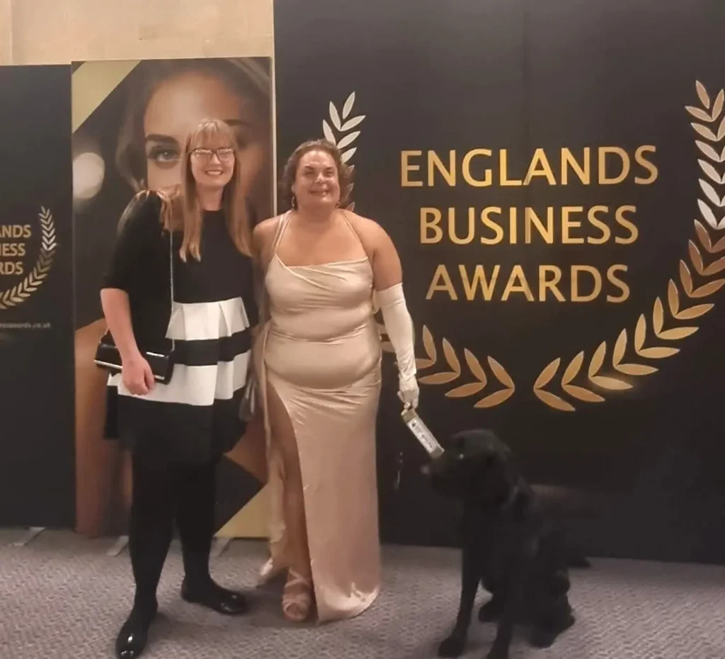 Sally Rodrigues at the 2026 England’s Business Awards, with Emily and guide dog Joe, in front of the awards backdrop